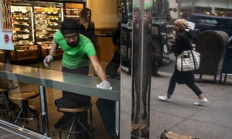 Nhân viên tại một cửa hàng bánh sandwich ở Manhattan, New York, lau chùi bàn cho khách. Ảnh: NYTimes.