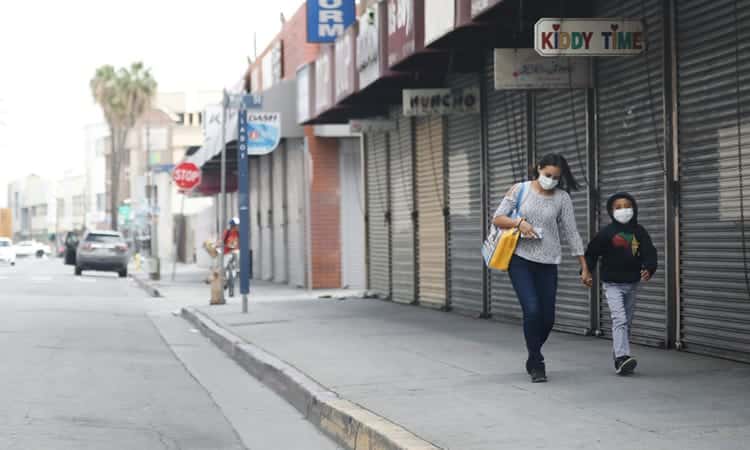 Người phụ nữ và bé trai đeo khẩu trang đi ngang những cửa hàng bị đóng cửa vì Covid-19 tại thành phố Los Angeles, bang California, Mỹ ngày 4/4. Ảnh: AFP.